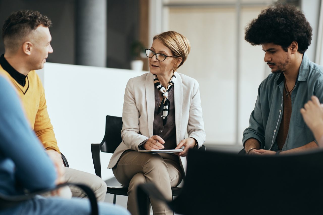 mature therapist talking to participants of group therapy at mental health center